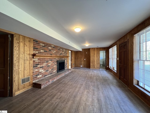 unfurnished living room with brick wall, wood walls, dark hardwood / wood-style floors, and a fireplace