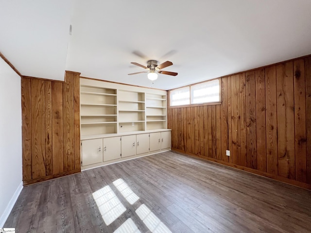 empty room with wood-type flooring, wood walls, and ceiling fan