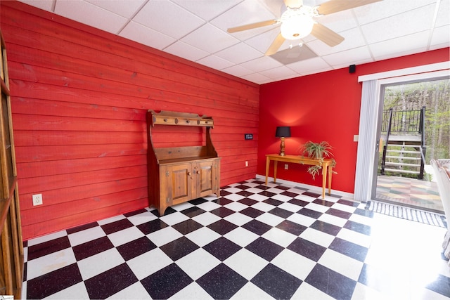 interior space featuring a drop ceiling, wood walls, and ceiling fan