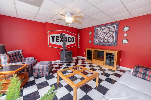 interior space featuring a wood stove, ceiling fan, and a paneled ceiling