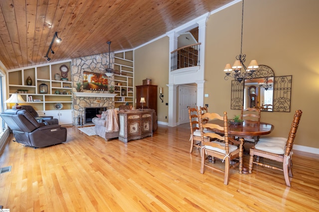 dining space with wood ceiling, wood-type flooring, a notable chandelier, a stone fireplace, and built in features