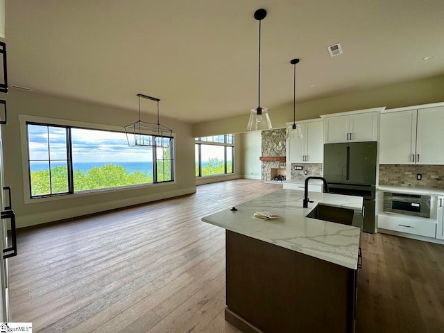 kitchen with white cabinetry, hanging light fixtures, tasteful backsplash, light stone counters, and a center island with sink