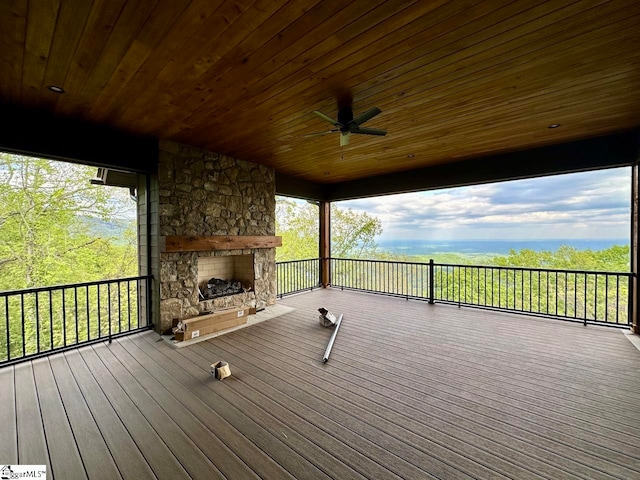 wooden deck with an outdoor stone fireplace and ceiling fan