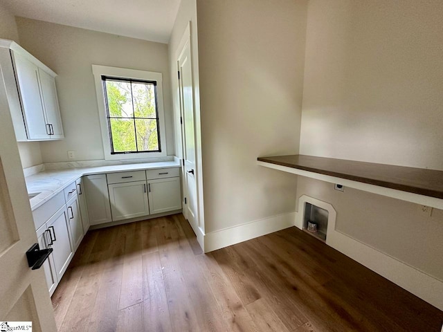 clothes washing area featuring electric dryer hookup, light hardwood / wood-style flooring, and cabinets