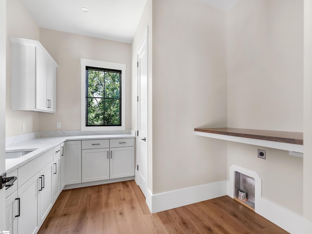 clothes washing area with cabinets, light wood-type flooring, hookup for an electric dryer, and sink