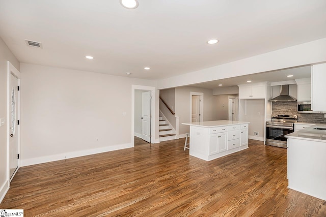 kitchen with a center island, white cabinetry, hardwood / wood-style floors, appliances with stainless steel finishes, and wall chimney range hood