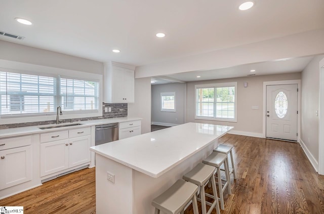 kitchen with white cabinets, sink, a kitchen bar, stainless steel dishwasher, and hardwood / wood-style flooring