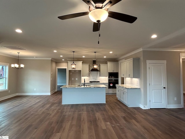 kitchen with pendant lighting, sink, built in microwave, an island with sink, and ceiling fan with notable chandelier