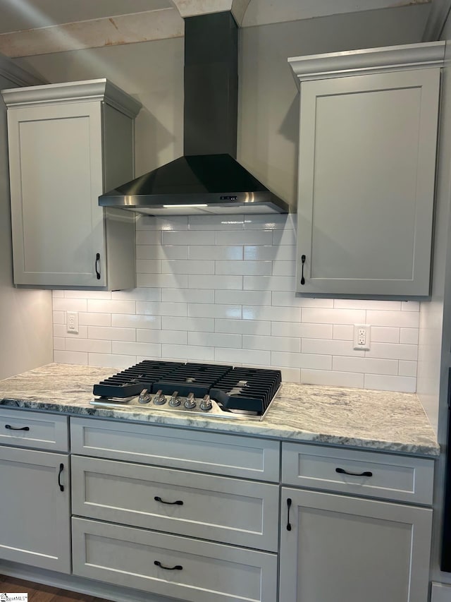 kitchen featuring decorative backsplash, light stone countertops, stainless steel gas cooktop, and wall chimney exhaust hood