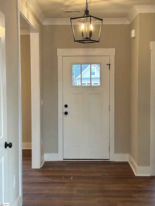 foyer entrance with dark wood-type flooring, ornamental molding, and a chandelier