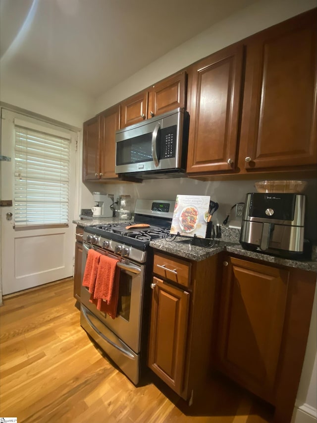 kitchen with dark stone counters, stainless steel appliances, and light wood-type flooring