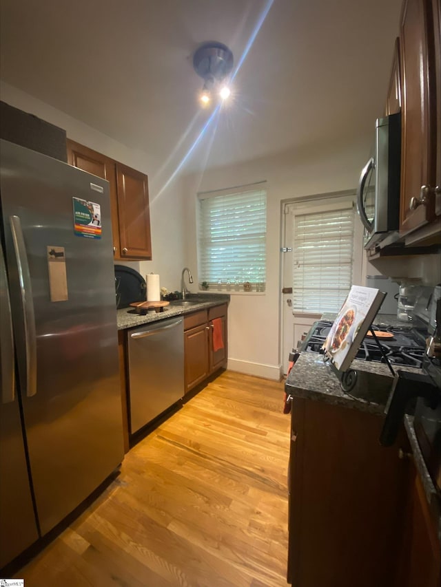 kitchen with stainless steel appliances, light hardwood / wood-style floors, sink, and dark stone countertops