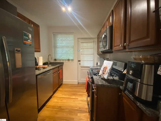 kitchen featuring stainless steel appliances, dark stone countertops, sink, and light wood-type flooring