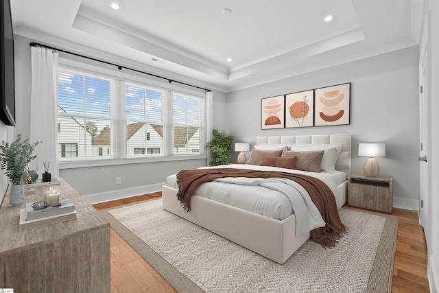 bedroom with a raised ceiling, ornamental molding, and light hardwood / wood-style floors