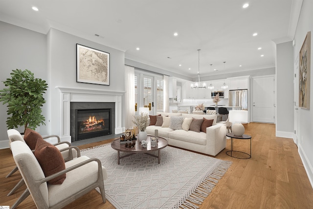 living room with crown molding, an inviting chandelier, and light hardwood / wood-style flooring