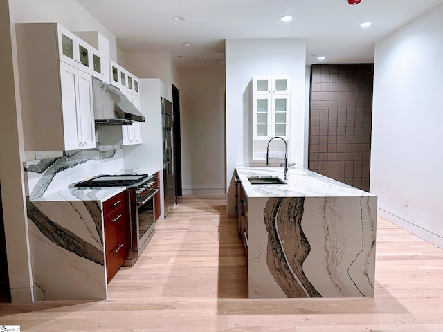 kitchen featuring high end stove, white cabinets, sink, light wood-type flooring, and light stone countertops