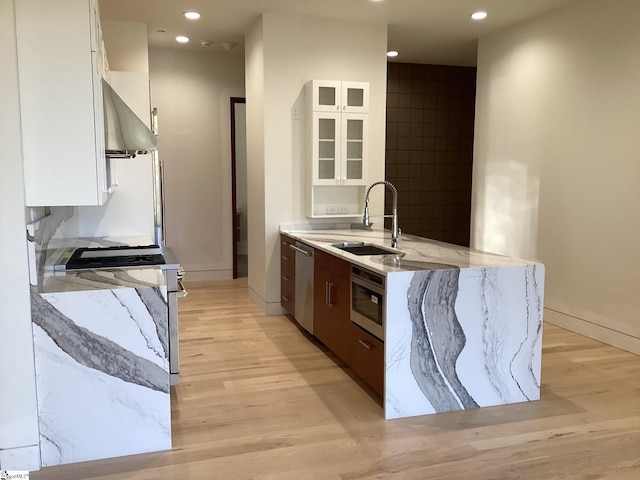 kitchen featuring wall chimney exhaust hood, sink, light hardwood / wood-style floors, white cabinetry, and stainless steel appliances