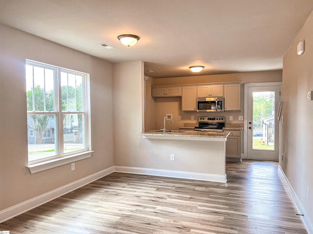 kitchen featuring light stone countertops, light wood-type flooring, kitchen peninsula, stainless steel appliances, and sink