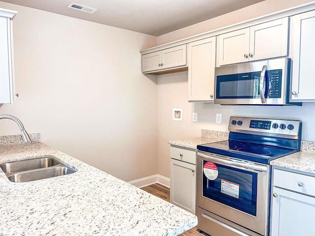 kitchen featuring appliances with stainless steel finishes, wood-type flooring, sink, and light stone counters