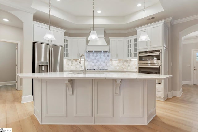 kitchen with premium range hood, a large island, appliances with stainless steel finishes, a raised ceiling, and tasteful backsplash