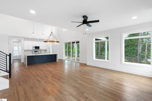 unfurnished living room with ceiling fan with notable chandelier, plenty of natural light, sink, and light hardwood / wood-style floors