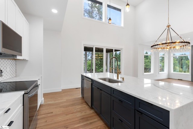 kitchen with appliances with stainless steel finishes, sink, white cabinetry, light hardwood / wood-style flooring, and pendant lighting