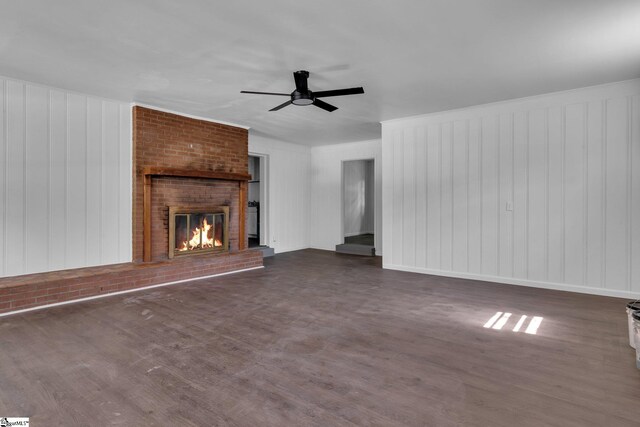 unfurnished living room featuring brick wall, a brick fireplace, dark hardwood / wood-style flooring, and ceiling fan