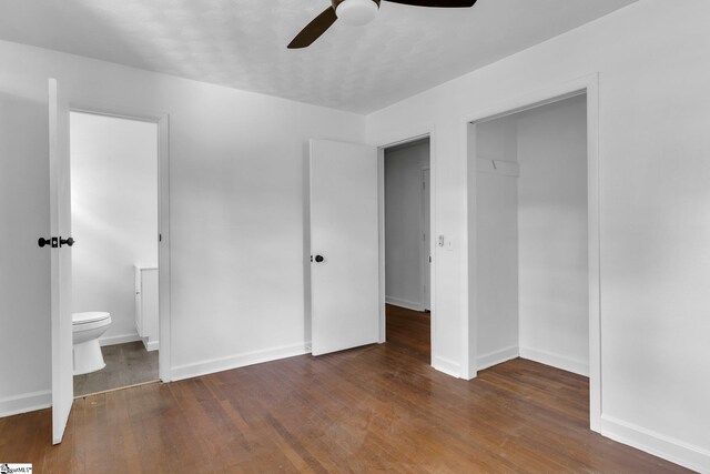 unfurnished bedroom featuring ceiling fan, a closet, dark wood-type flooring, connected bathroom, and a walk in closet