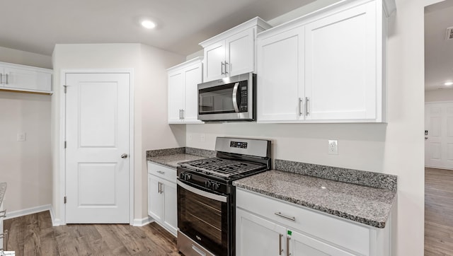 kitchen featuring white cabinets, stainless steel appliances, light hardwood / wood-style flooring, and dark stone counters