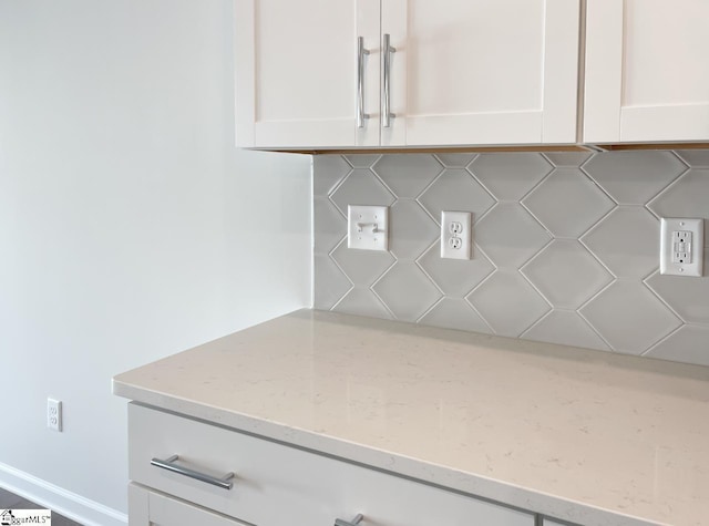 room details featuring backsplash, white cabinetry, and light stone countertops