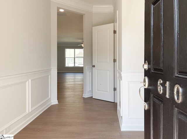 entrance foyer with wood finished floors, a decorative wall, wainscoting, crown molding, and ceiling fan