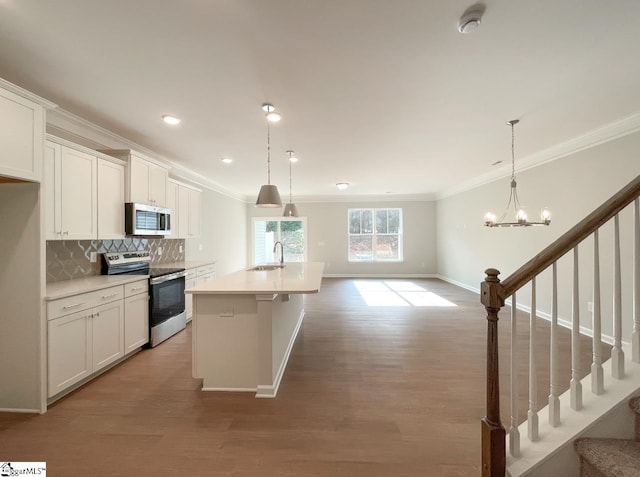 kitchen featuring white cabinetry, appliances with stainless steel finishes, decorative light fixtures, and an island with sink