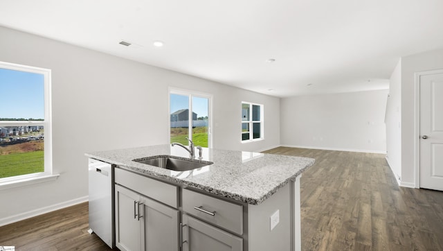 kitchen with gray cabinetry, sink, light stone counters, stainless steel dishwasher, and an island with sink