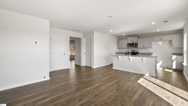 kitchen featuring a kitchen island with sink, light stone counters, dark hardwood / wood-style floors, and appliances with stainless steel finishes