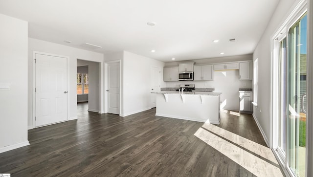 kitchen with a kitchen bar, light stone counters, an island with sink, dark hardwood / wood-style flooring, and stainless steel appliances