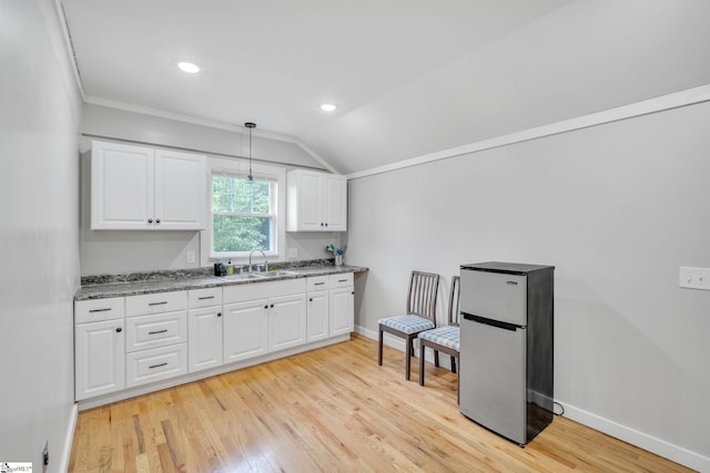 kitchen with decorative light fixtures, stainless steel refrigerator, white cabinetry, light wood-type flooring, and sink