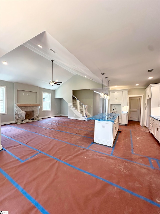 kitchen featuring lofted ceiling, a center island, white cabinets, baseboards, and ceiling fan