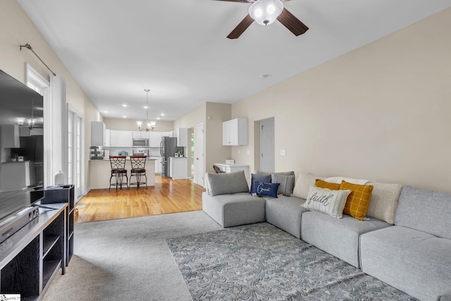 carpeted living room with ceiling fan with notable chandelier