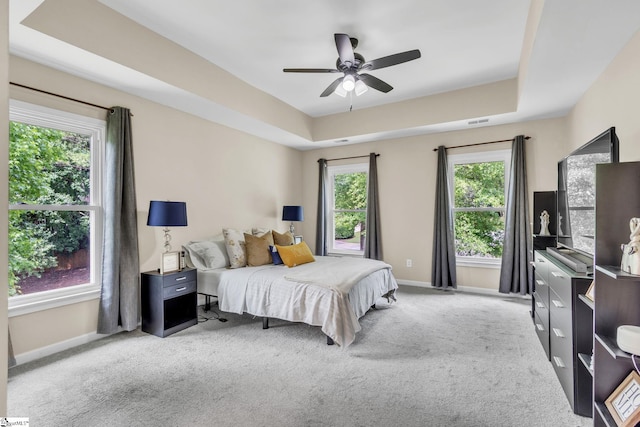 carpeted bedroom with a raised ceiling and ceiling fan