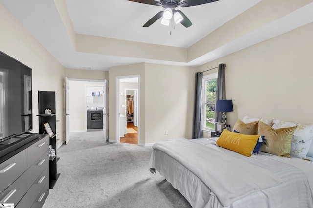 carpeted bedroom with a tray ceiling, connected bathroom, and ceiling fan