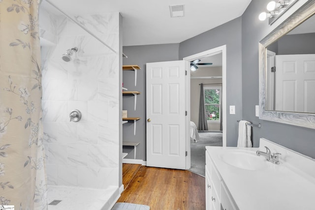 bathroom with vanity with extensive cabinet space, ceiling fan, tiled shower, and wood-type flooring