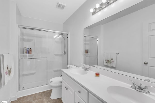 bathroom featuring tile flooring, a shower with door, dual bowl vanity, and toilet