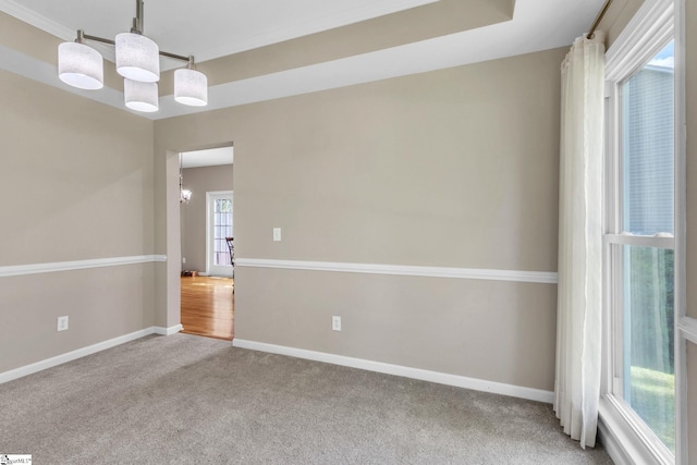 carpeted spare room with a notable chandelier, crown molding, and a raised ceiling