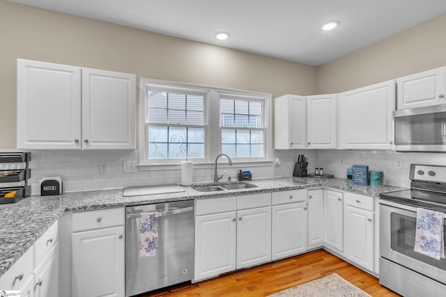 kitchen featuring stainless steel appliances, tasteful backsplash, white cabinetry, light wood-type flooring, and sink