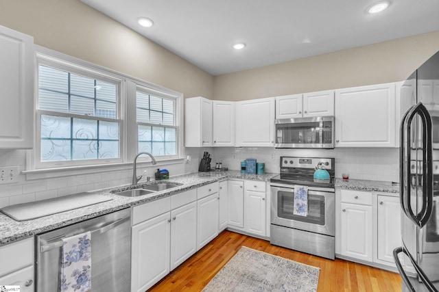 kitchen with sink, light hardwood / wood-style floors, backsplash, and appliances with stainless steel finishes