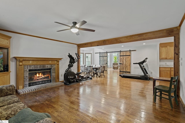 workout room featuring a fireplace, ceiling fan, hardwood / wood-style floors, a barn door, and ornamental molding