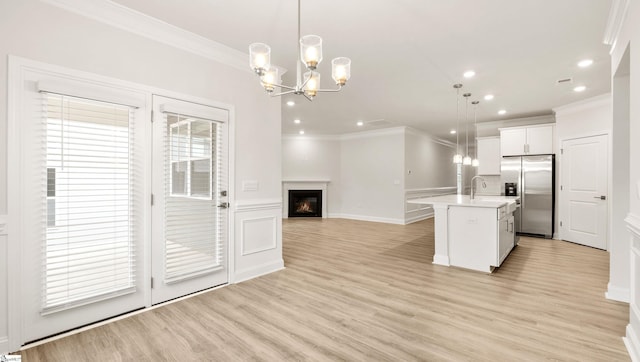 kitchen with decorative light fixtures, stainless steel fridge, ornamental molding, and a center island with sink