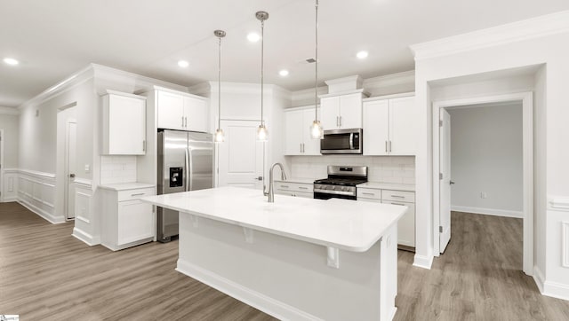 kitchen with decorative light fixtures, stainless steel appliances, white cabinets, and a center island with sink