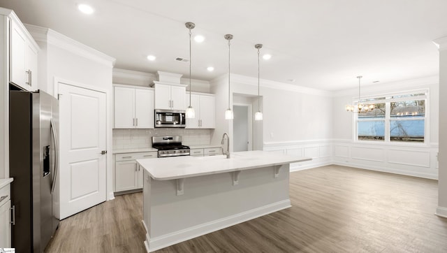 kitchen with appliances with stainless steel finishes, a kitchen island with sink, white cabinets, a kitchen bar, and decorative light fixtures