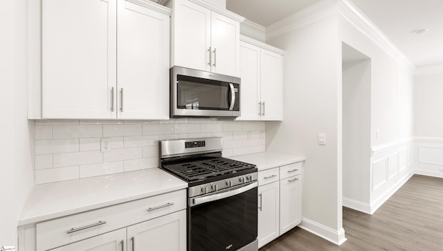 kitchen featuring hardwood / wood-style flooring, white cabinetry, stainless steel appliances, tasteful backsplash, and ornamental molding